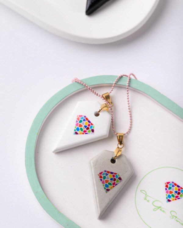 Concrete gem pendants with colorful logo design on pink and gold chains displayed on a white and mint green background